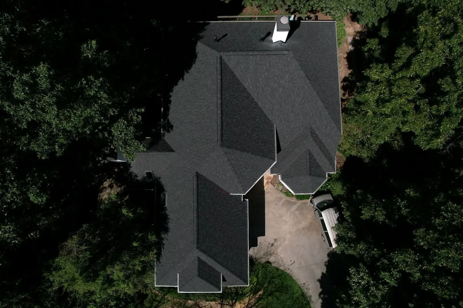 Inspection photo of a dark shingle roof under heavy tree cover