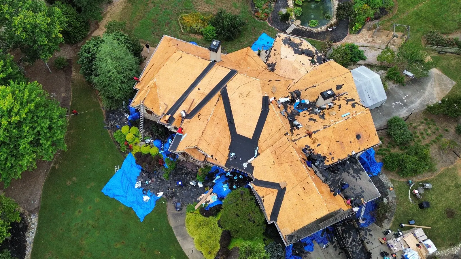 View of a Dryco tear-off with new decking exposed and blue tarps protecting the landscaping